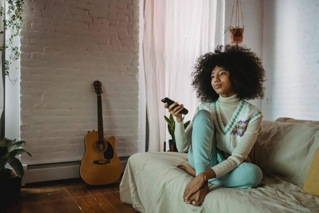 black woman with natural hair sits on the couch holding a television remote