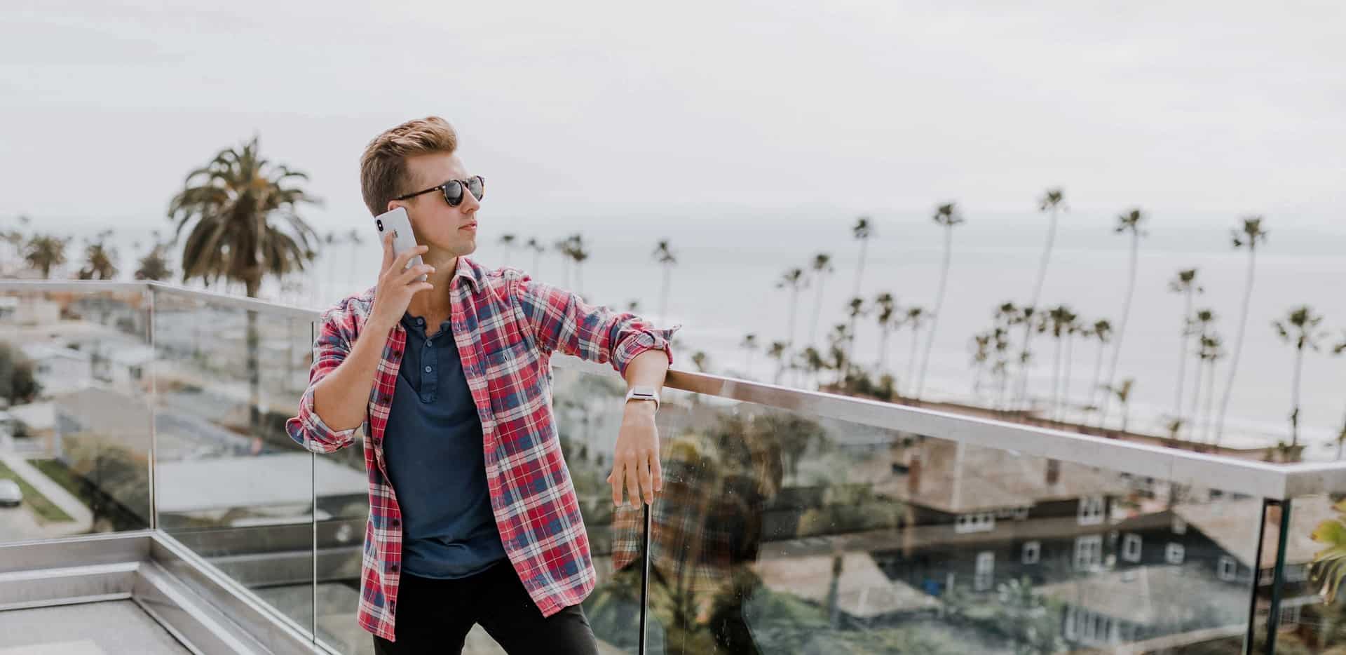 ceo of a startup stands on the balcony of an oceanfront building with his cell phone held to his ear