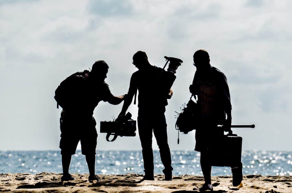 Silhouette of three men with camera equipment against an ocean background
