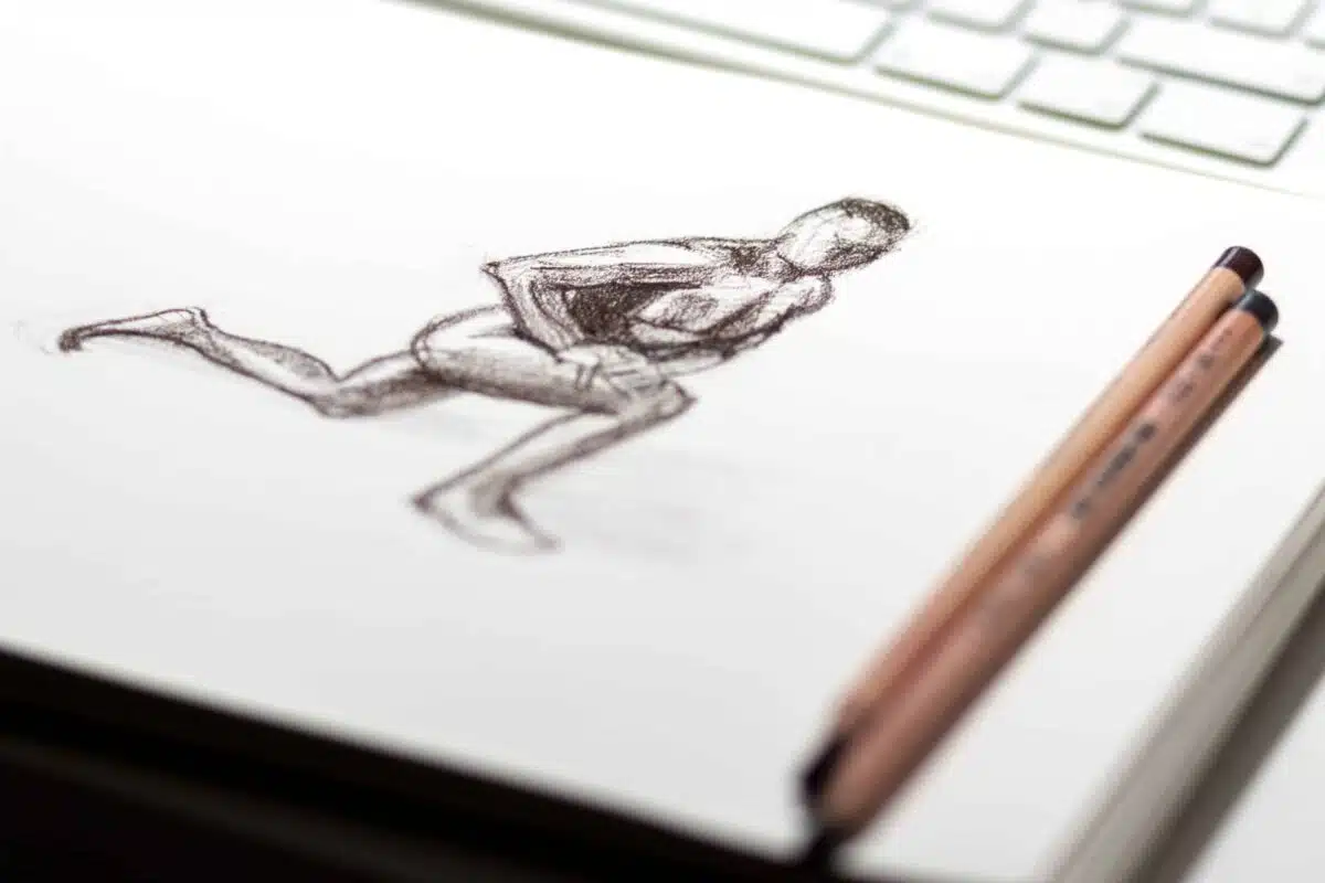 A sketch of a kneeling human figure, inspired by Richard Williams, is drawn on white paper, with two pencils resting nearby. The edge of a computer keyboard is visible in the background.