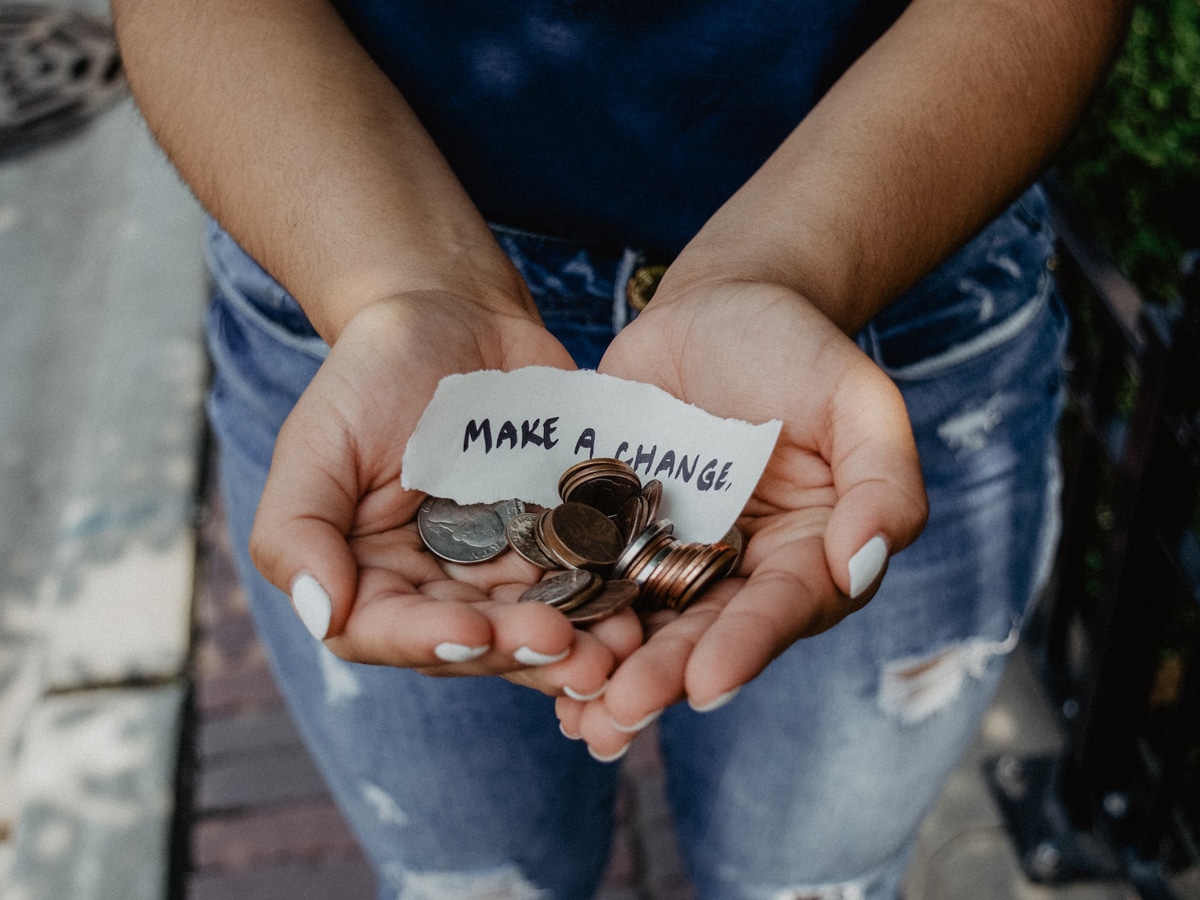 open hands hold a pile of coins and a note that says "make a change"