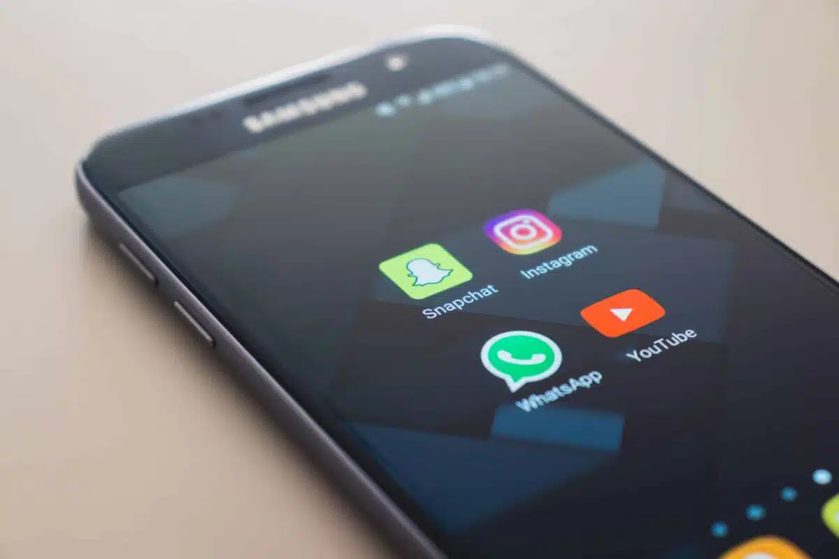 A Samsung smartphone displays the Snapchat, Instagram, WhatsApp, and YouTube app icons—perfect for sharing ephemeral video moments—against a soft beige background.