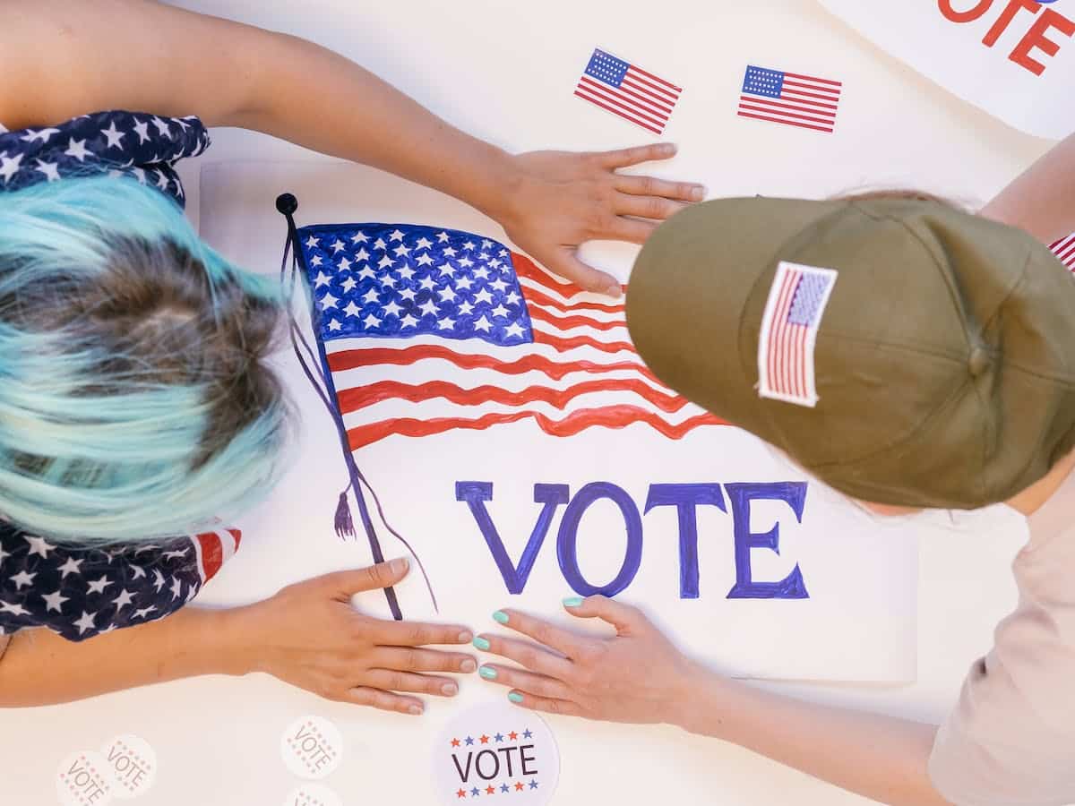 Two activists prepare a campaign poster that says VOTE and features a flag