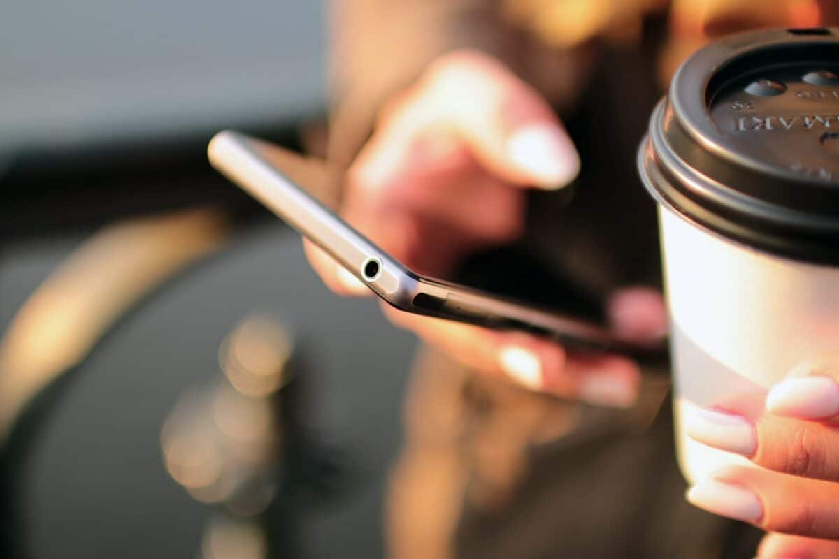 Woman looks at cell phone while holding coffee
