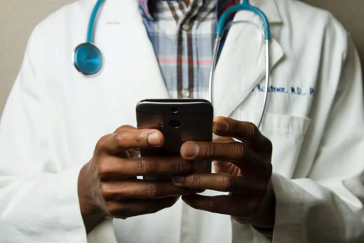 We see a doctor with a stethoscope looking at his smartphone.