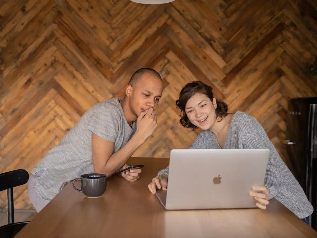 two people lean across a table to view a video on a laptop screen